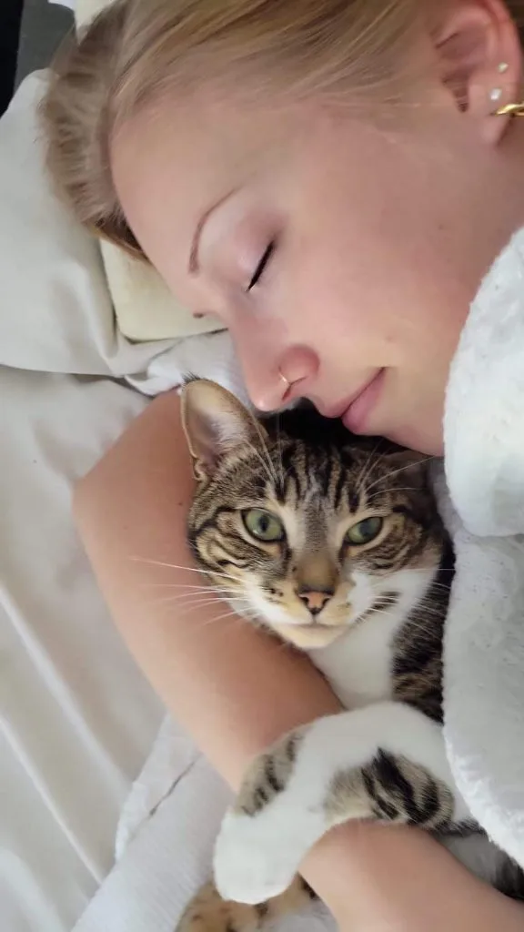 A woman sleeping peacefully with her cat curled up in her arms