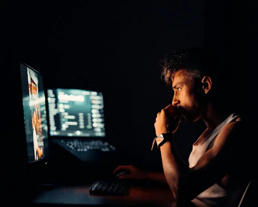 A man concentrating at a computer late at night, lit only by the monitor