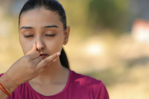 A woman practicing a nasal breathing exercise outdoors, eyes closed, fingers resting lightly on her nose